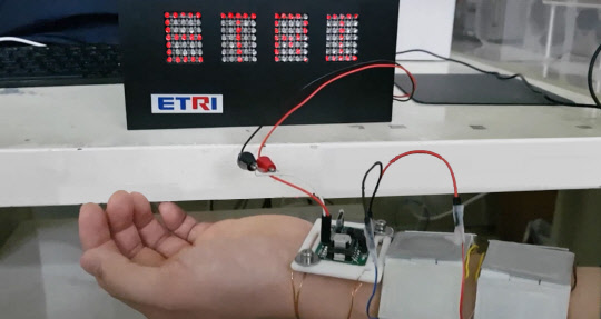 ETRI 연구자가 체온을 기반으로 전원을 공급하는 착용형 열전소자를 피부에 부착해 LED 전광판으로 'ETRI'라는 붉은색 글씨를 점등하고 있다.  ETRI 제공